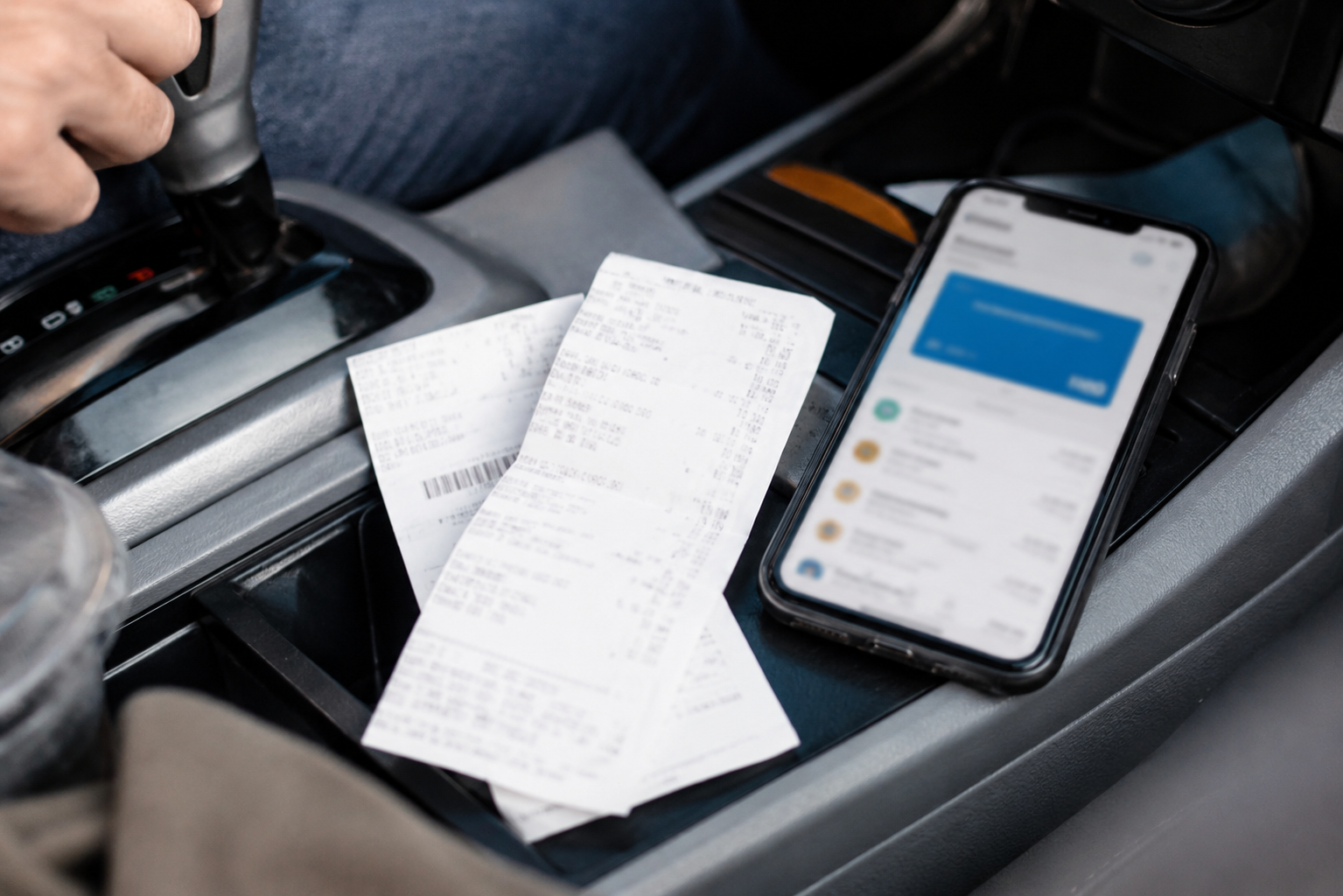 Gas and grocery receipts sit beside a phone with a blurred payment app screen.