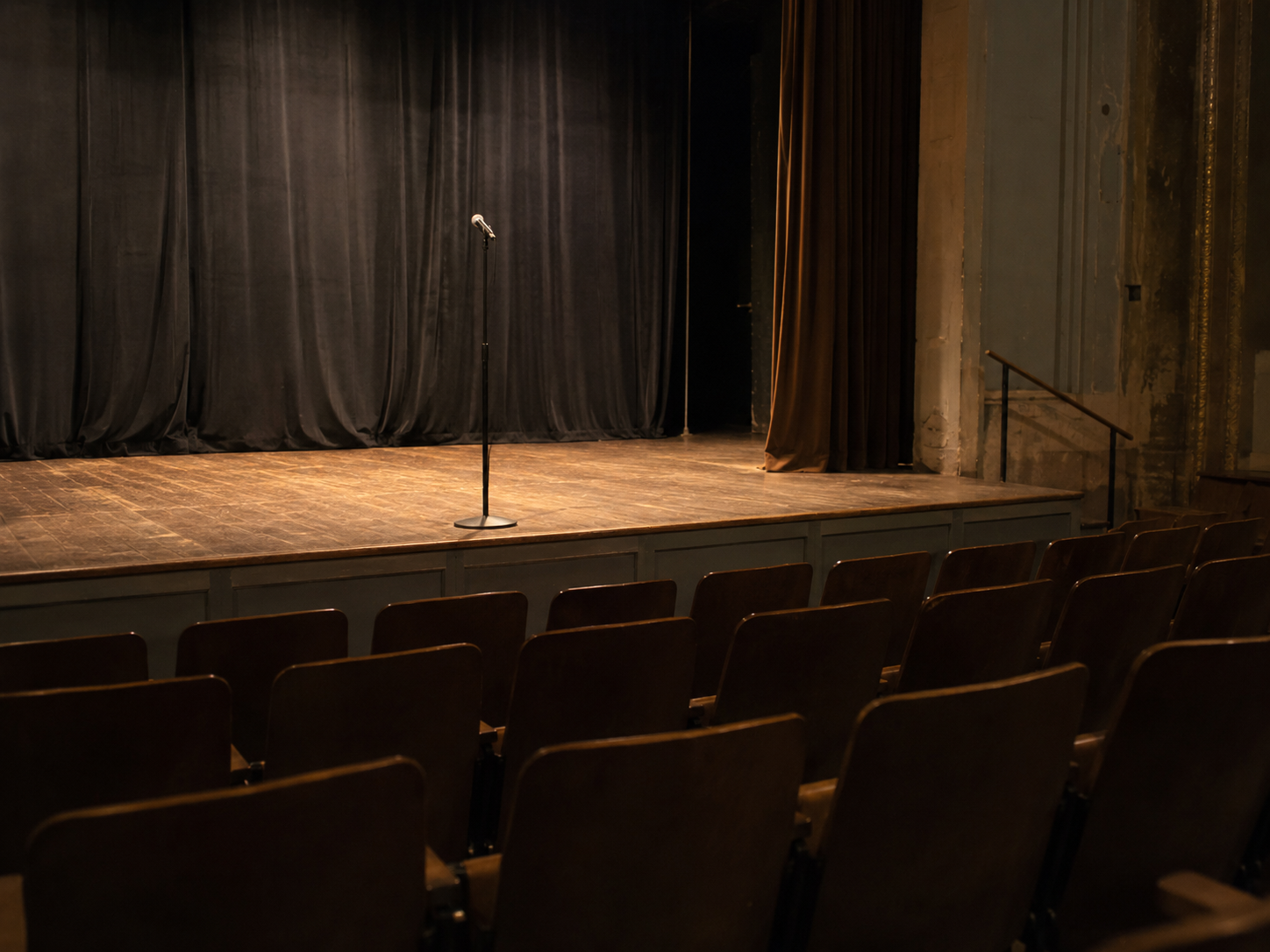 An empty theater stage with a microphone stand under warm lights.