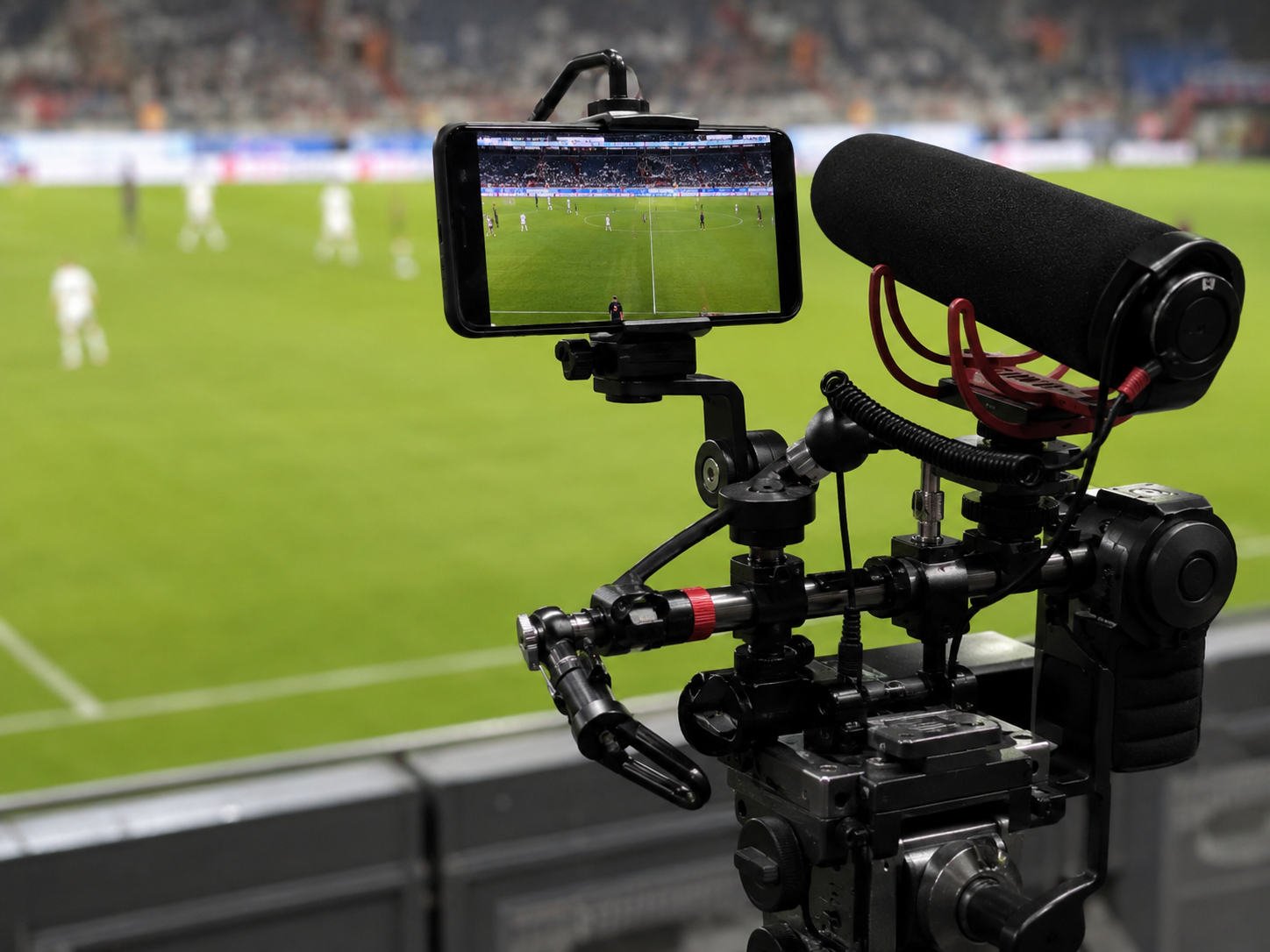 A smartphone mounted on a professional video rig near a soccer field.