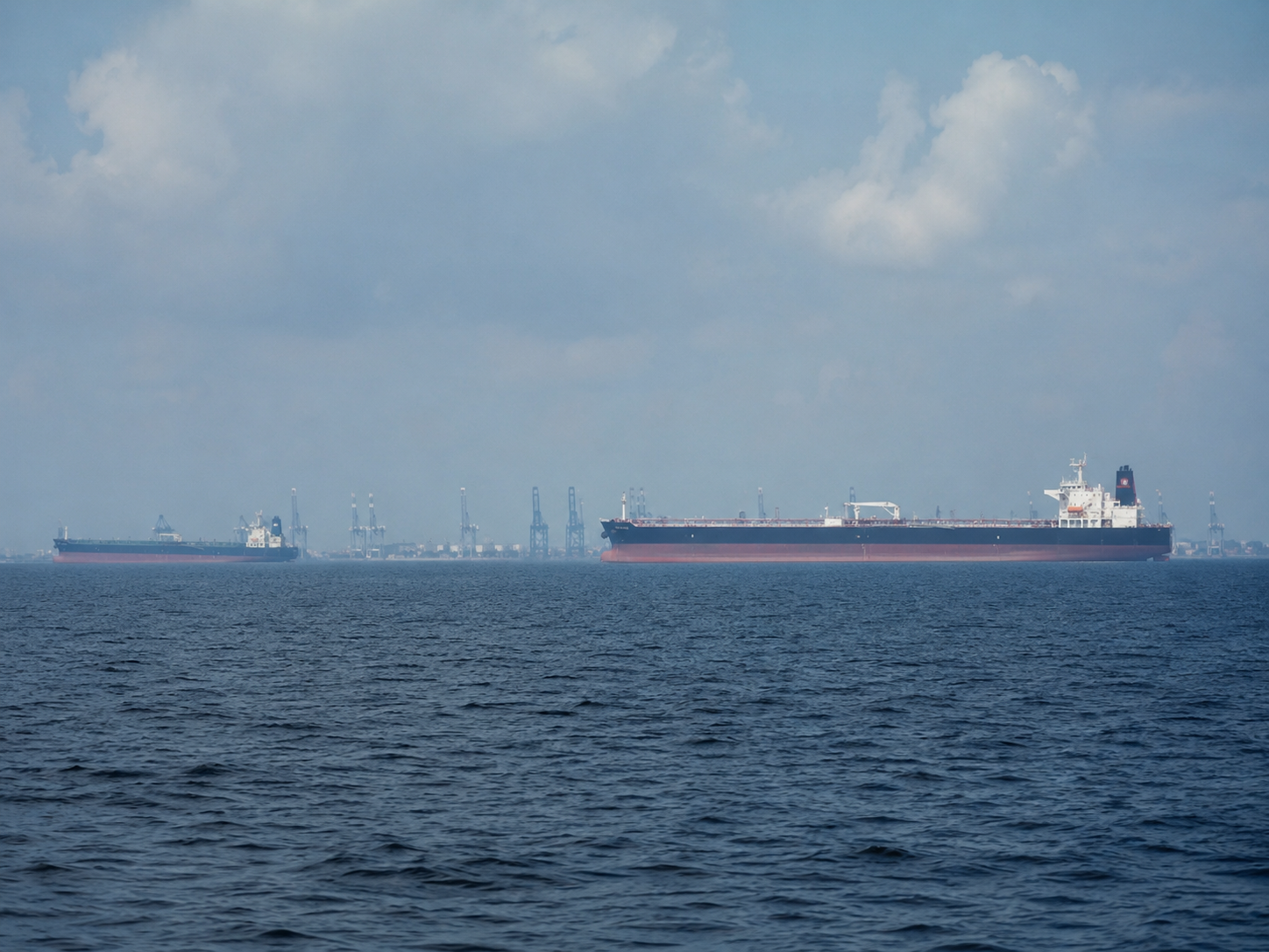 Oil tankers near a port route under hazy skies.