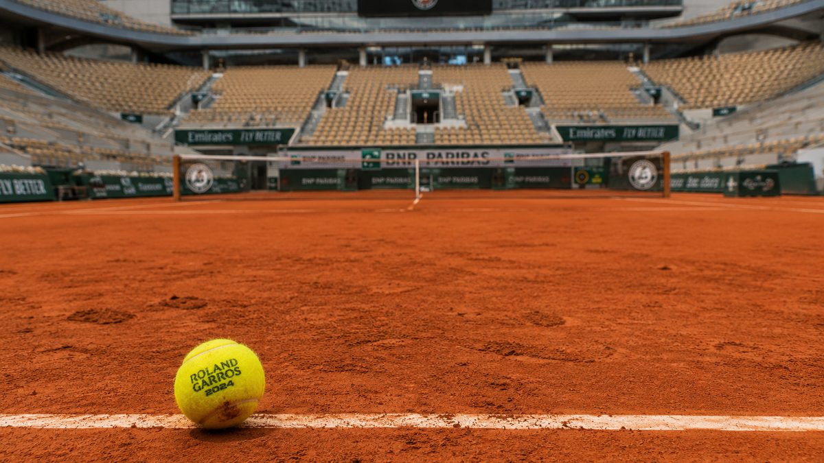 A tennis ball rests near the baseline on an empty clay court.