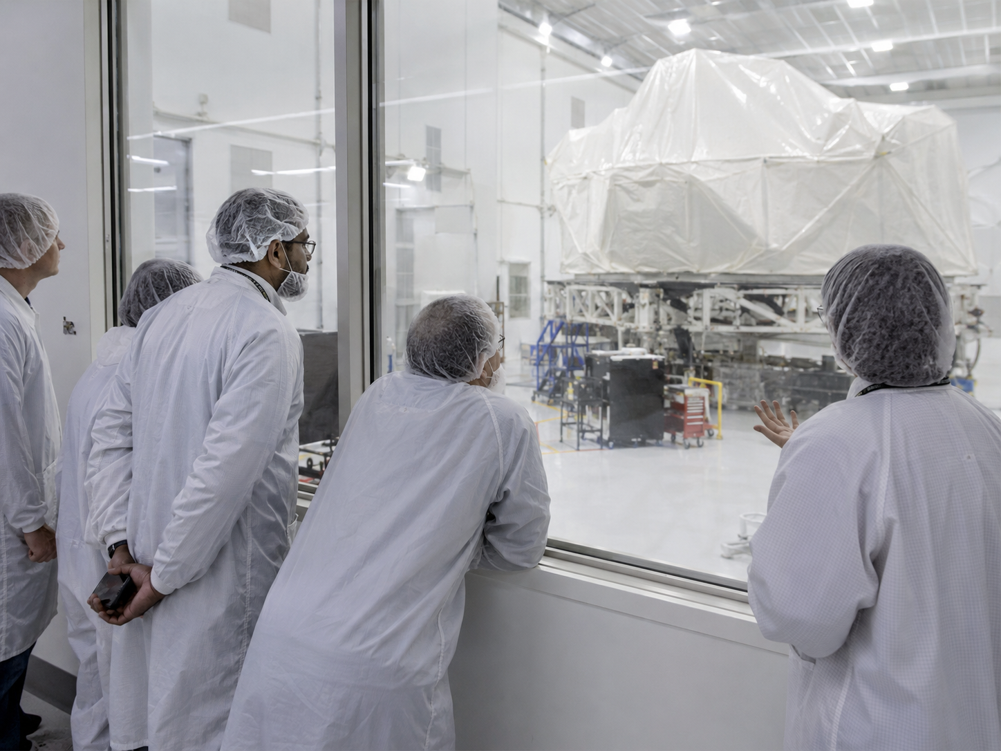 Engineers observe a covered space telescope component inside a clean room.
