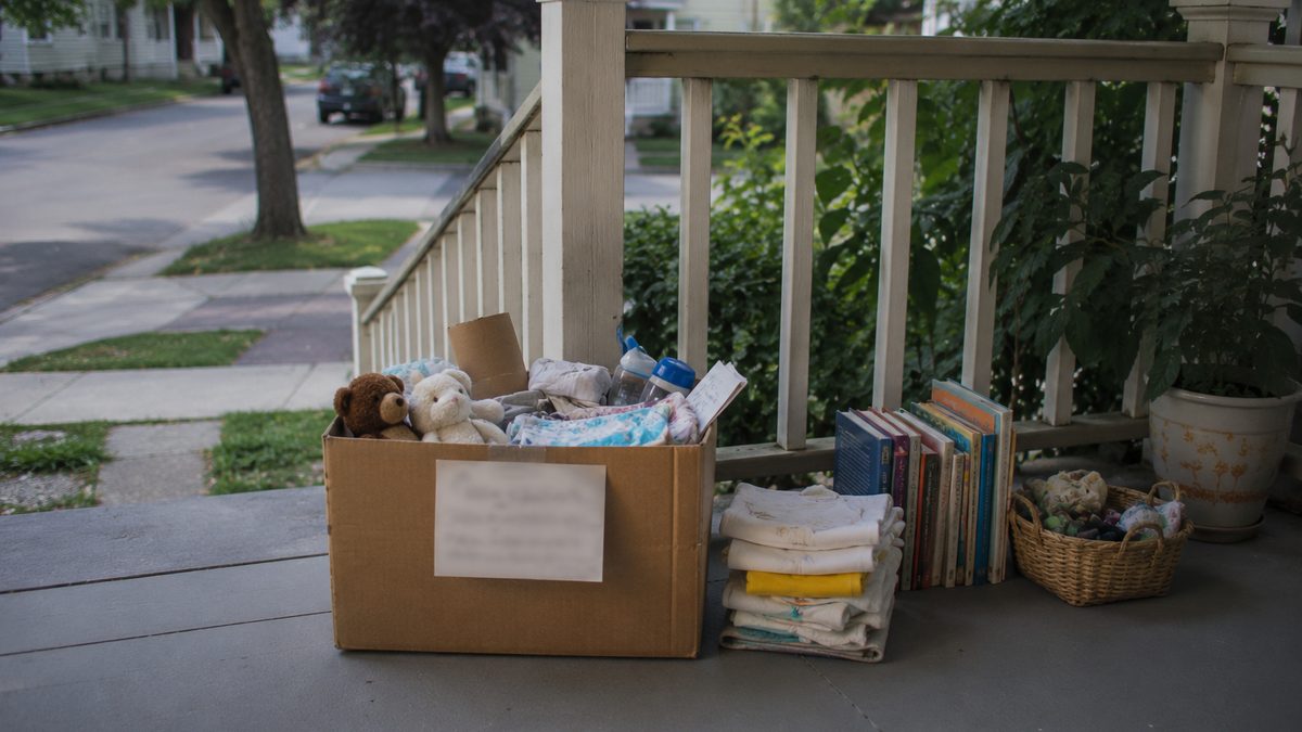 A porch pickup box with household items, folded clothes, and books set out for neighbors.