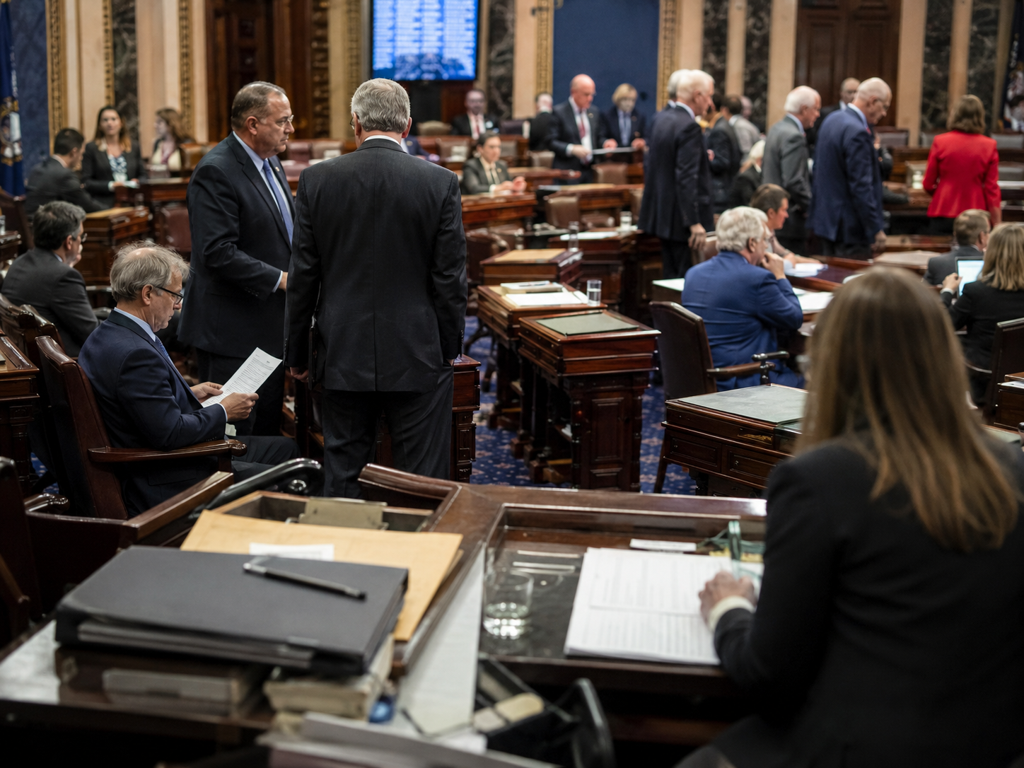 An empty congressional hearing room with folders and microphones represents a delayed vote.