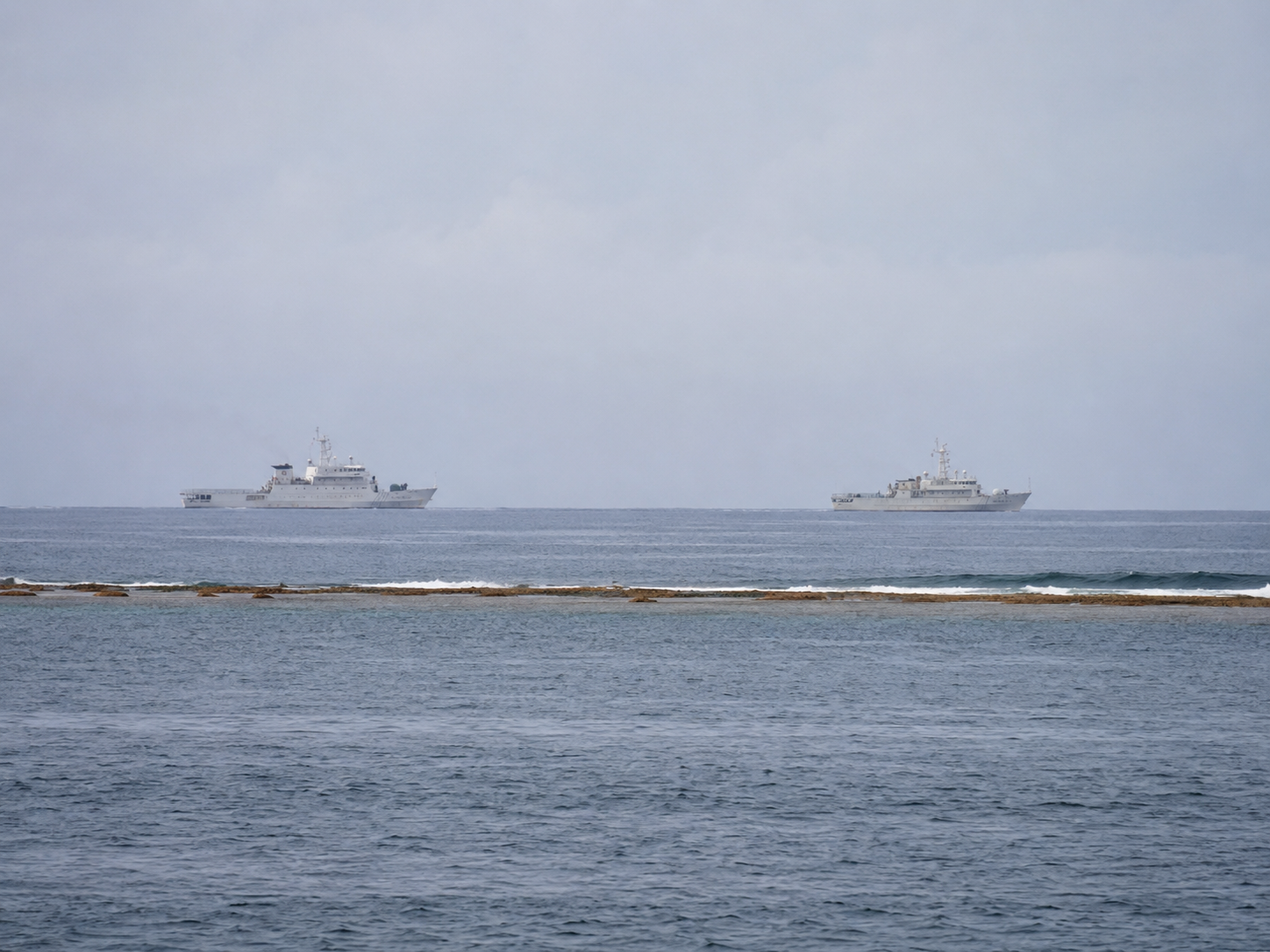 Two coast guard vessels patrol open water near a distant reef.