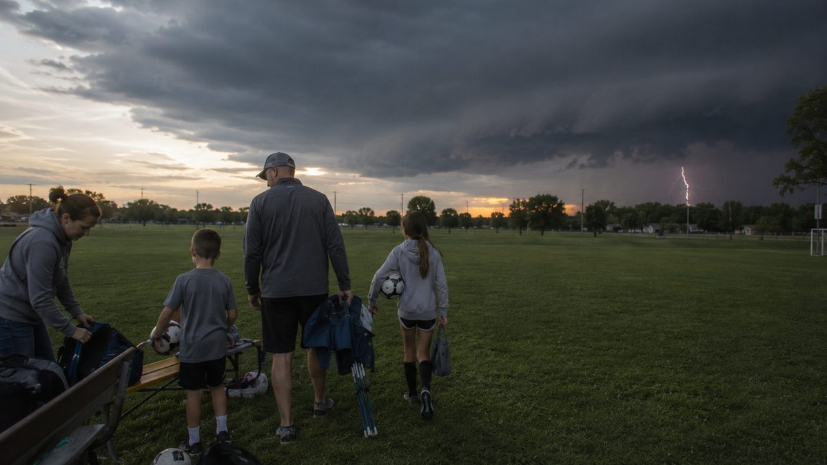 People leaving a sports field as a distant thunderstorm approaches.