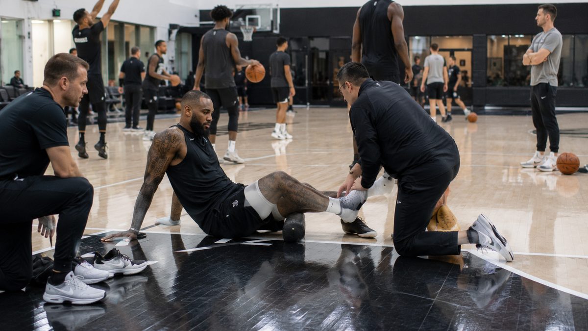 A basketball player works with trainers during practice while teammates train nearby.