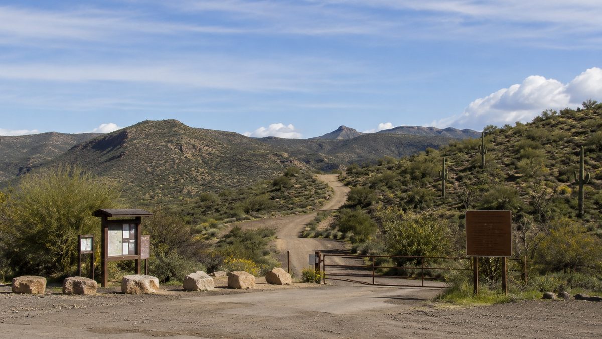 Federal public lands trailhead with a dirt road and distant hills.