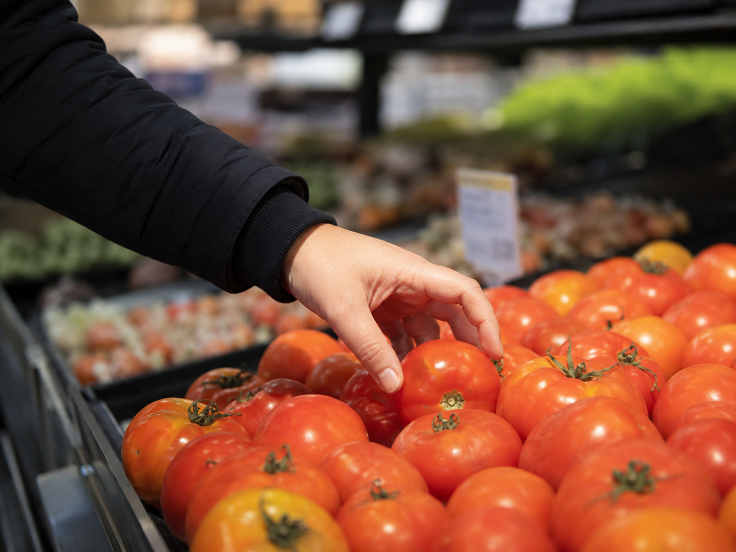 Tomatoes sit in a grocery produce section with a blurred price tag nearby.